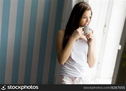 Pretty young woman with cup of coffee by the window
