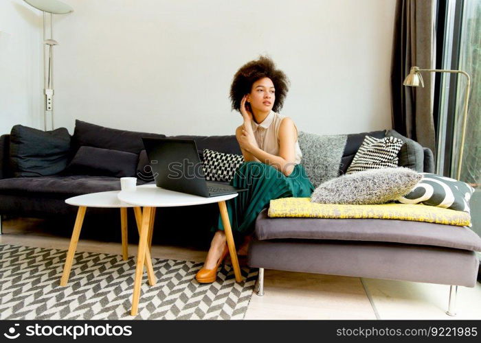 Pretty young woman with curly hair, uses  laptop and sitting on the sofa at home