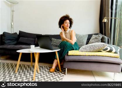 Pretty young woman with curly hair, uses  laptop and sitting on the sofa at home
