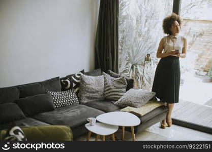 Pretty young woman with curly hair using mobile phone by the window at home