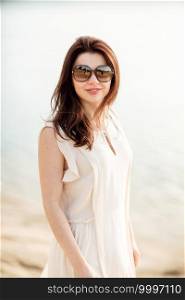 Pretty young woman with dark hair near at the beach near the lake in dress and sunglasses. concept of happy holiday and resort time.. Pretty young woman with dark hair near at the beach near the lake in dress and sunglasses. concept of happy holiday and resort time
