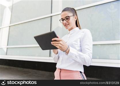 Pretty young woman with digital tablet by the office building wall