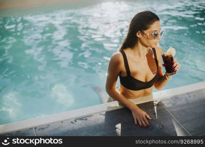 Pretty young woman with drink on the poolside at hot summer day