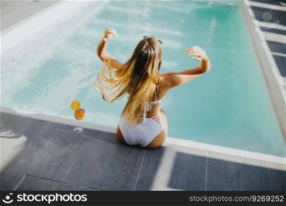 Pretty young woman with drink on the poolside at hot summer day