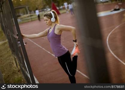 Pretty young woman with earphones stretching during sport training