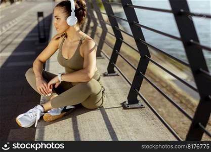 Pretty young woman with earphones takes a break after running in the urban area