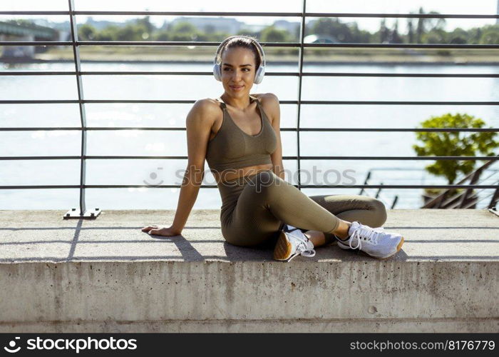 Pretty young woman with earphones takes a break after running in the urban area