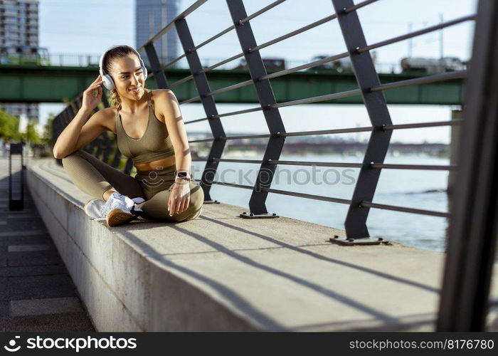 Pretty young woman with earphones takes a break after running in the urban area