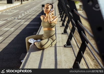 Pretty young woman with earphones takes a break after running in the urban area