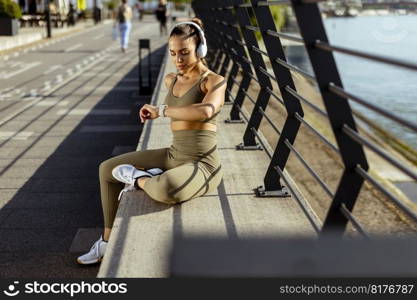 Pretty young woman with earphones takes a break after running in the urban area