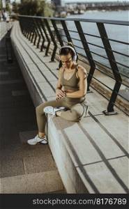 Pretty young woman with earphones takes a break after running in the urban area