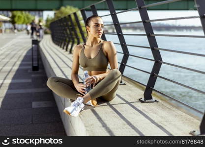 Pretty young woman with earphones takes a break after running in the urban area