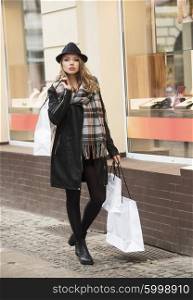 pretty young woman with hat and scarf walking on the street shop , she bring some shopper with her .