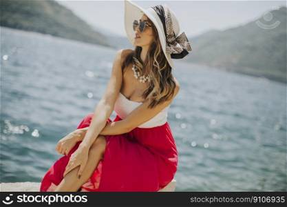 Pretty young woman with hat and sunglasses sitting by the sea
