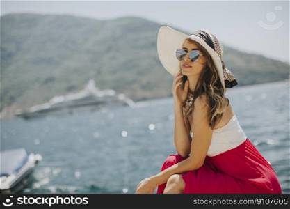 Pretty young woman with hat and sunglasses sitting by the sea