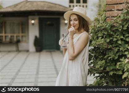 Pretty young woman with hat drinking cold lemonade in the resort garden