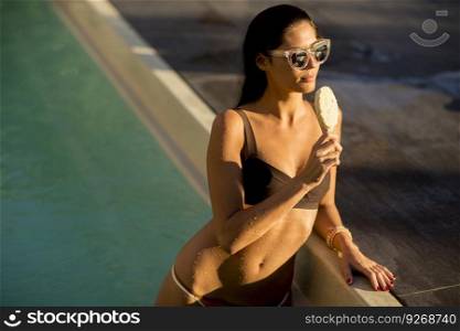 Pretty young woman with ice cream on the poolside at hot summer day