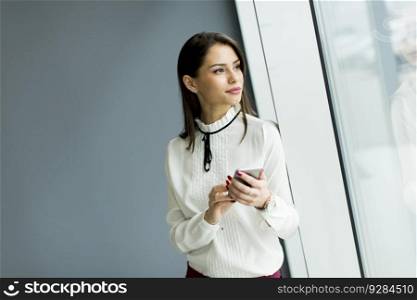 Pretty young woman with mobile phone by gray wall in the office