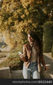 Pretty young woman with mobile phone in the park on sunny autumn day