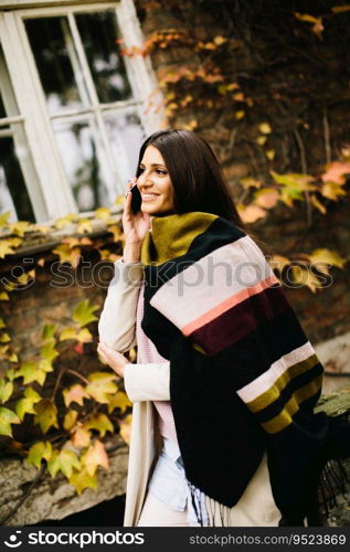 Pretty young woman with mobile phone on street at autumn day