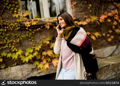 Pretty young woman with mobile phone on street at autumn day