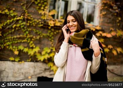 Pretty young woman with mobile phone on street at autumn day