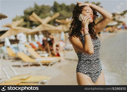 Pretty young woman with mobile phone on the beach at hot summer day