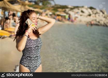 Pretty young woman with mobile phone on the beach at summer