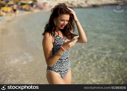 Pretty young woman with mobile phone on the beach at summer