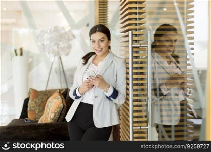Pretty young woman with mobile phone standing in the modern office