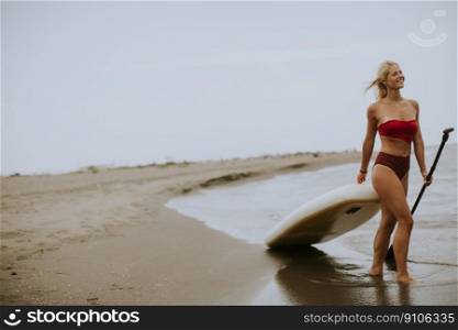Pretty young woman with paddle board on the beach on a summer day