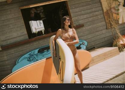Pretty young woman with paddle board on the beach on a summer day
