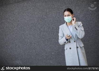 Pretty young woman with protective facial mask on the street using mobile phone