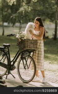 Pretty young woman with white bichon frise dog in the basket of electric bike