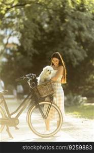 Pretty young woman with white bichon frise dog in the basket of electric bike