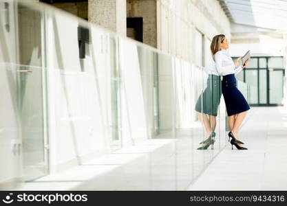 Pretty young woman working on digital tablet in the office hallway