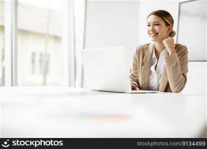 Pretty young woman working on laptop in bright office with big screen behind her