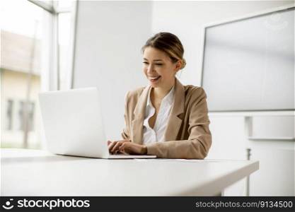 Pretty young woman working on laptop in bright office with big screen behind her