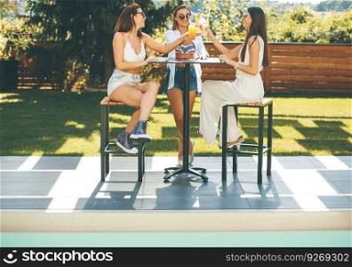 Pretty young women drinking coctail and having fun by the pool at hot summer day