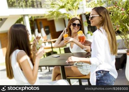 Pretty young women drinking coctail and having fun by the swimming pool at hot summer day