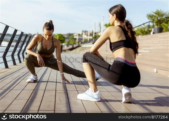 Pretty young women in sportswear exercising on a river promenade