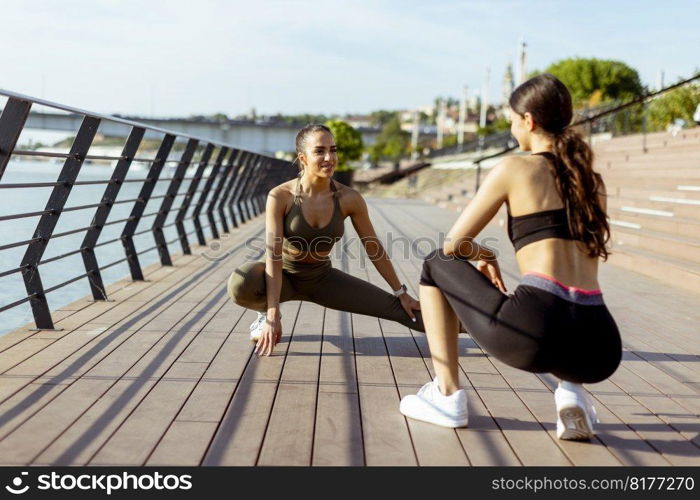 Pretty young women in sportswear exercising on a river promenade