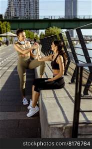 Pretty young women in sportswear taking a rest after exercising on a river promenade