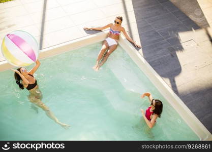 Pretty young women playing with ball in swimming pool on a summer day