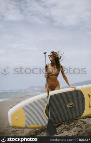 Pretty young women with paddle board on the beach on a summer day
