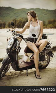 Pretyy young woman riding scooter on a beach