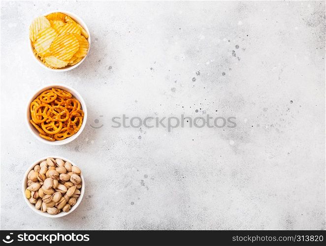 Pretzel and potato crisps and pistachio in white ceramic bowl on stone kitchen background. Space for text. Snack for beer