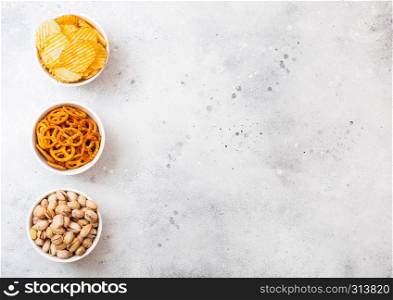 Pretzel and potato crisps and pistachio in white ceramic bowl on stone kitchen background. Space for text. Snack for beer