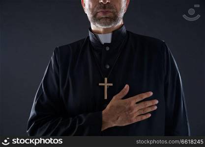 Priest hand in heart gesture with cross on black background