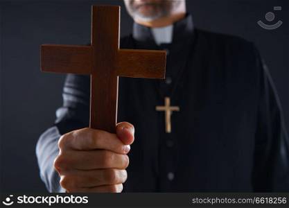 Priest holding cross of wood praying in foreground